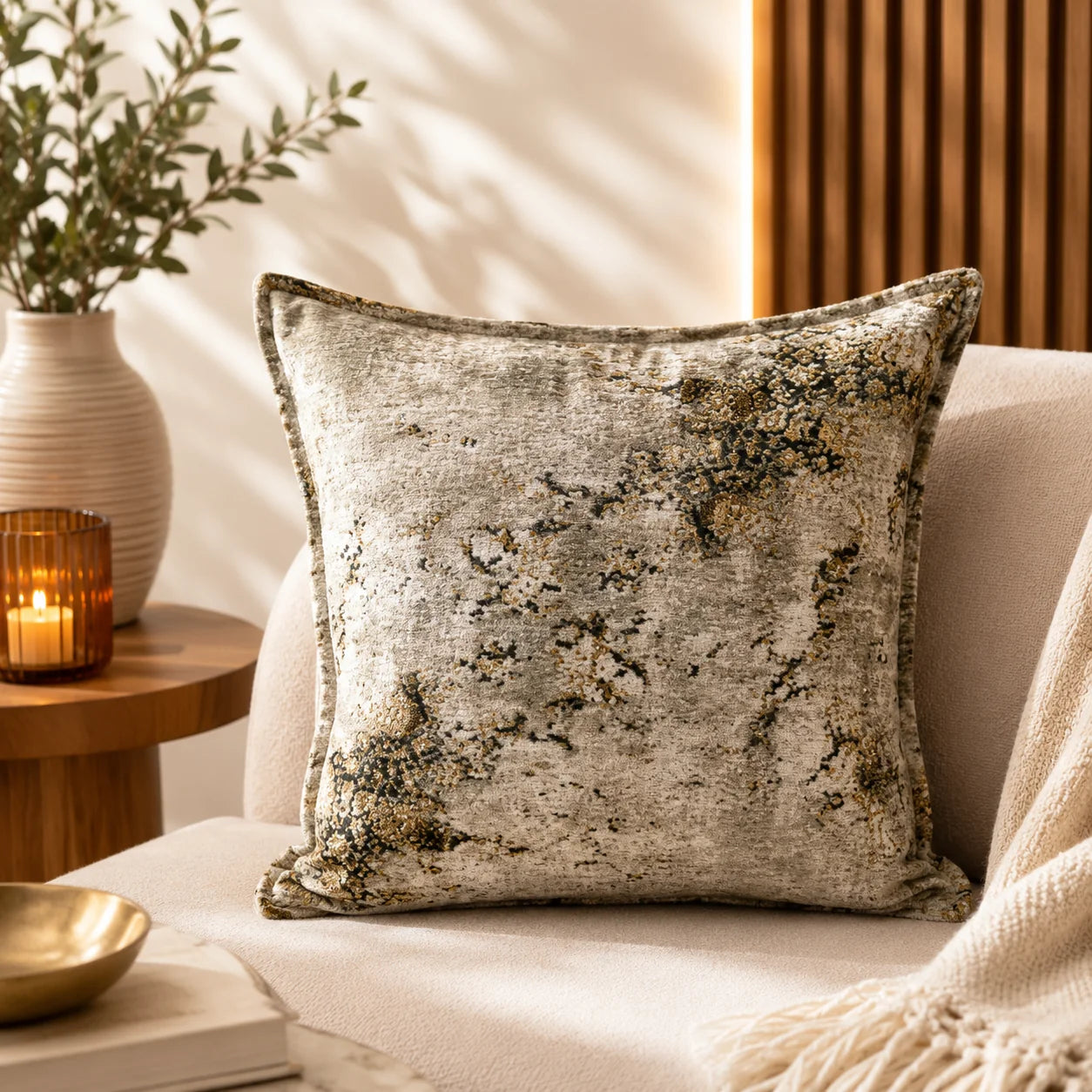 Almohadón de chenille de textura marmolada en tonos arena y beige con motas oliva y doradas