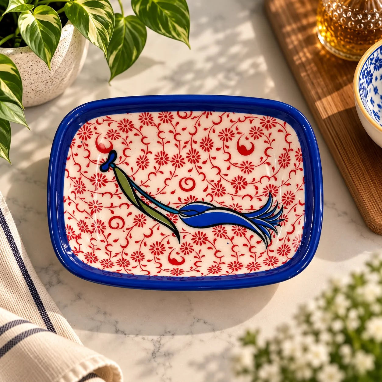 Plato de cerámica con borde azul, fondo de flores rojas y tulipán central azul verdoso