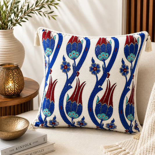 Almohadón con motivo tradicional de tulipanes turcos bordados en azul cobalto y rojo sobre fondo marfil, con borlas crema en las esquinas