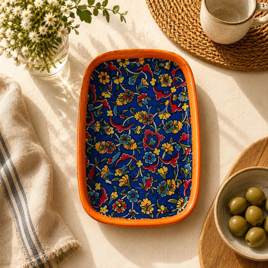 Bandeja con flores rojas, amarillas y azules densas sobre fondo azul intenso y borde naranja