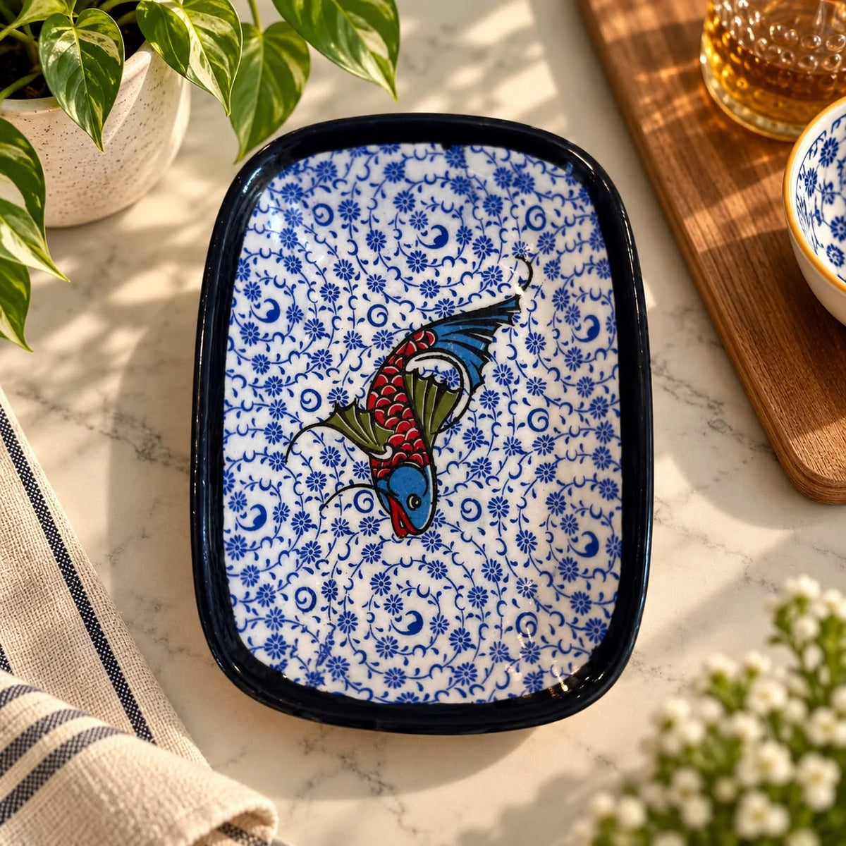 Bandeja blanca con estampado floral azul fino y un pez rojo, azul y verde en el centro, borde negro