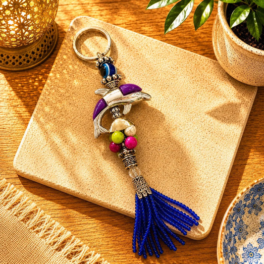 Llavero Delfín Violeta: Delfín metálico plateado con detalle violeta, cuentas multicolor y borla azul.