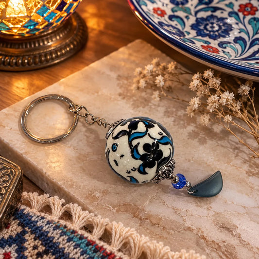 Llavero Ojo Turco Cerámica Pintada: Bola de cerámica blanca pintada a mano con motivo floral azul, colgante en forma de gota.