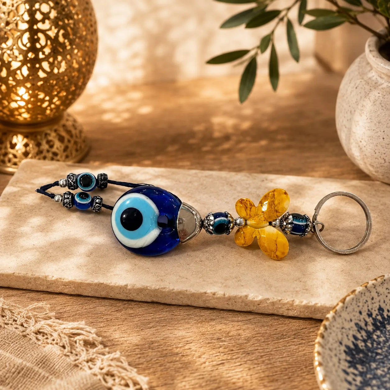 Llavero Ojo Turco Flor Mostaza: Ojo turco azul junto a una flor facetada color mostaza y dorado.