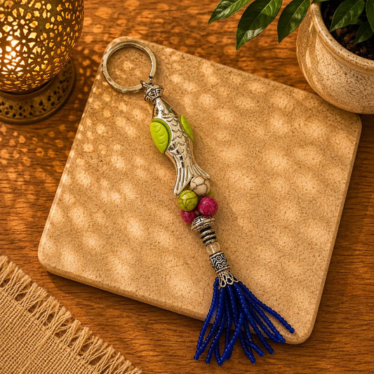 Llavero Pez Multicolor: Pez metálico plateado con hojas verde lima y cuentas rosa, blanco y verde, borla azul.